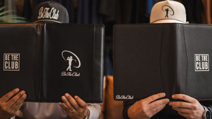 Two people holding black folders with 'Be The Club' logo.