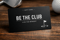 Gift card with 'Be the Club' branding on a wooden surface with golf-themed items.